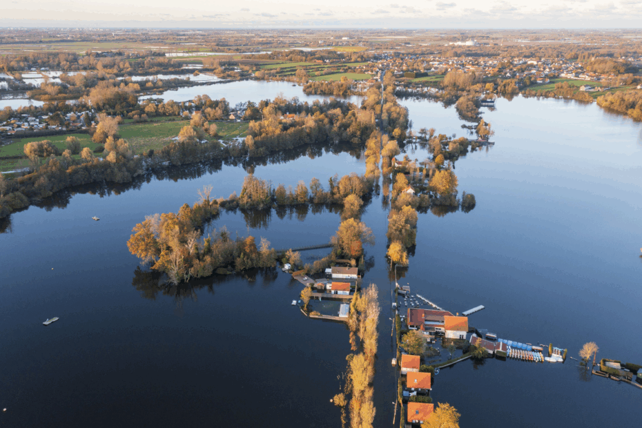 Vue aérienne d’une vaste zone inondée avec des maisons, des routes et des arbres partiellement submergés au coucher du soleil.