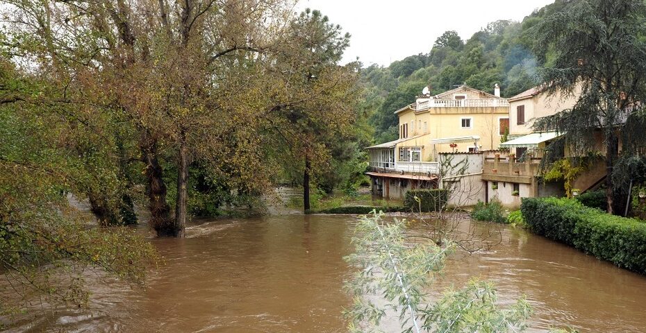 Photographie d’une zone inondée a Ajaccio avec de l’eau boueuse entourant des arbres et une maison située en bordure, dans un environnement verdoyant.