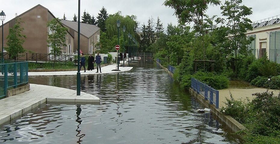 Rue résidentielle inondée avec des habitants observant les dégâts et des trottoirs submergés