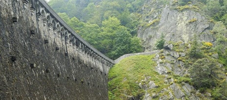 Vue d’un barrage en pierre en montagne entouré de végétation.
