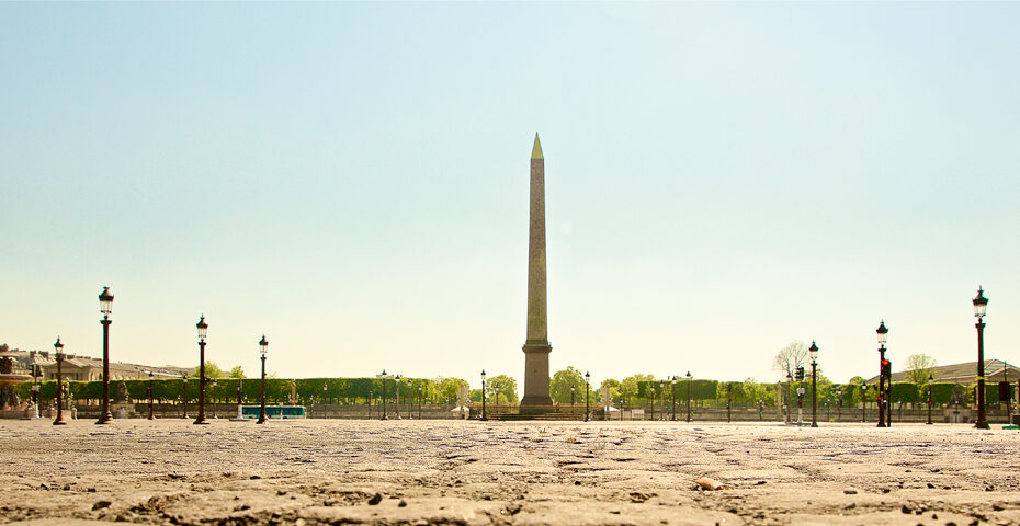 L'obélisque de la place de la Concorde à Paris vu depuis le sol, entouré de lampadaires, sous un ciel dégagé.