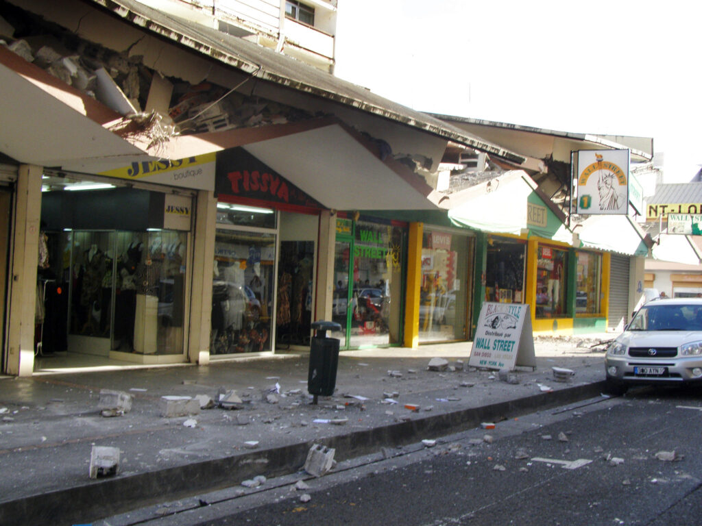 Scène de dégâts urbains en Martinique après le séisme de novembre 2007 : façades de magasins effondrées, débris au sol et structures fragilisées illustrant l’ampleur du tremblement de terre.
